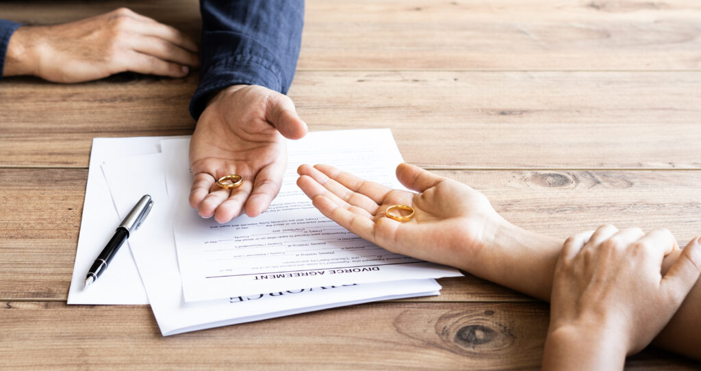 Couples' hands holding wedding rings over divorce papers